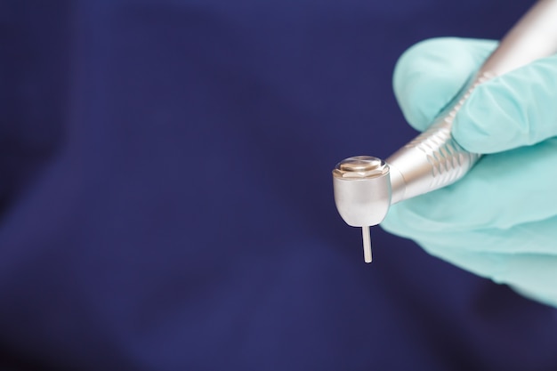 Close-up dentist's hand in a latex glove with high-speed dental handpiece on blurred background. Medical tools concept. Shallow depth of fiel.