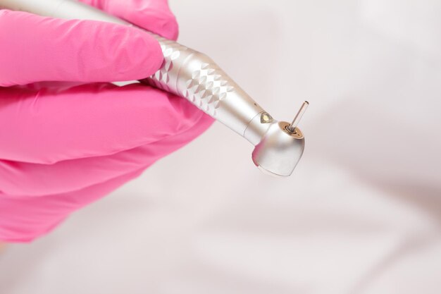 Foto primo piano della mano del dentista in un guanto in lattice rosa con manipolo dentale ad alta velocità in sfondo sfocato. concetto di strumenti medici. profondità di campo ridotta.