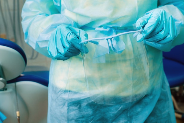 Close up of a dentist's hands holding a protective plastic screen in his office.