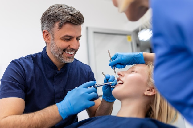 Close up of dentist's hands holding tool and syringe in hands Pain killer in action Female client keep mouth opened Beautiful smile and white teeth Cut view