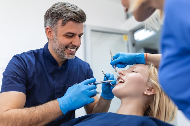 Primo piano delle mani del dentista che tengono lo strumento e la siringa nelle mani antidolorifico in azione il cliente femminile tiene la bocca aperta bel sorriso e denti bianchi vista tagliata