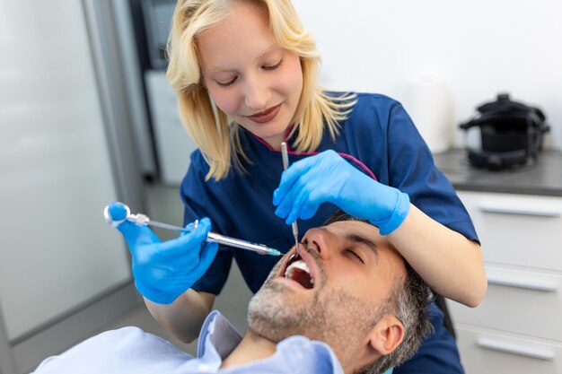 Close up of dentist's hands holding tool and syringe in hands Pain killer in action Male client keep mouth opened Beautiful smile and white teeth Cut view