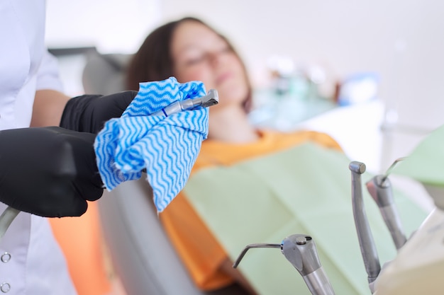 Foto primo piano del dentista che tratta gli strumenti, ragazza che si siede nella sedia che tratta i denti, mani di medici che preparano lo strumento disinfettante