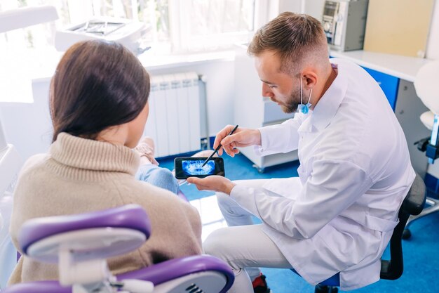 Photo close up of dentist with phone showing teeth xray to female pat