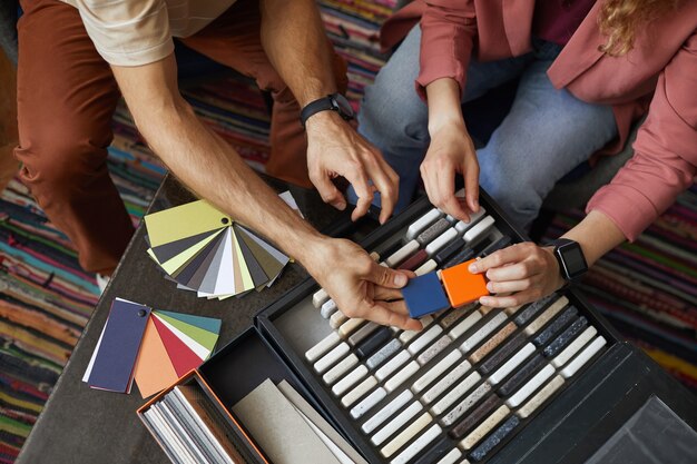 Close-up of designer sitting at the table with patterns and searching for the suitable color for the wall