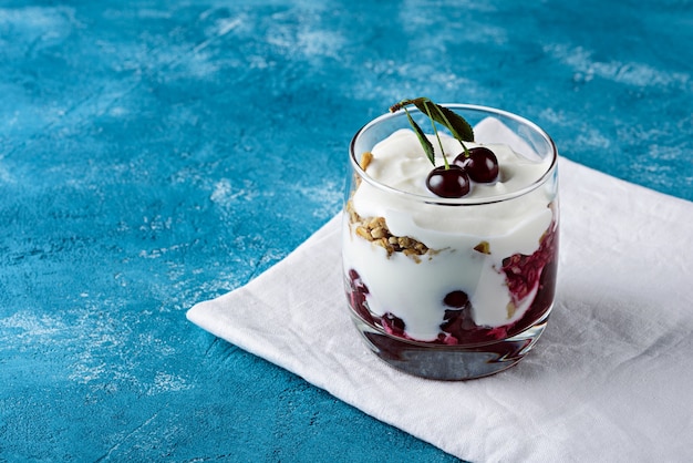 Close up of dessert with cherries, granola and cottage cheese in glass on white napkin