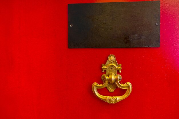 Close up detail of bright red door with golden ornate knocker and blank name plate