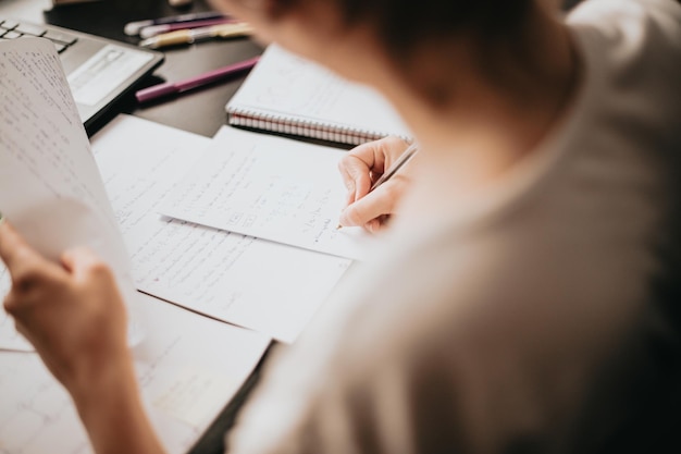 Close up detail image of a young woman studying and working on his home desk doing homework during university preparing for exam with textbook and taking notes selective focus on the pencil