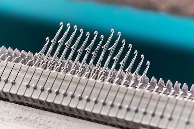 Close up detail of a line of raised steel latch needles on a commercial knitting machine in a knitwear factory