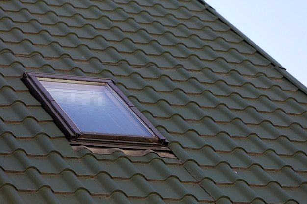 Close-up detail of new small attic plastic window installed in dark green shingled house roof