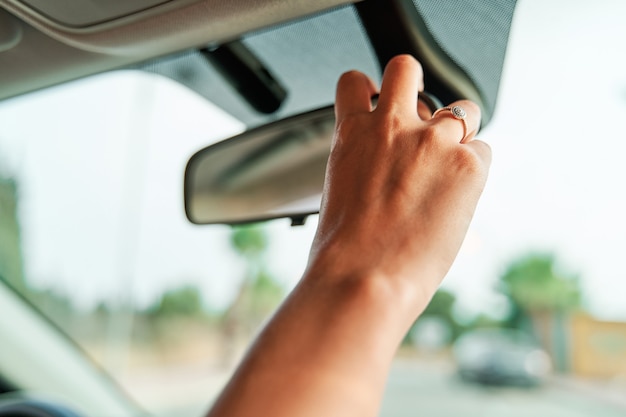 Close-up detail shot van de hand van een onherkenbare vrouw die de achteruitkijkspiegel in de auto aanpast.