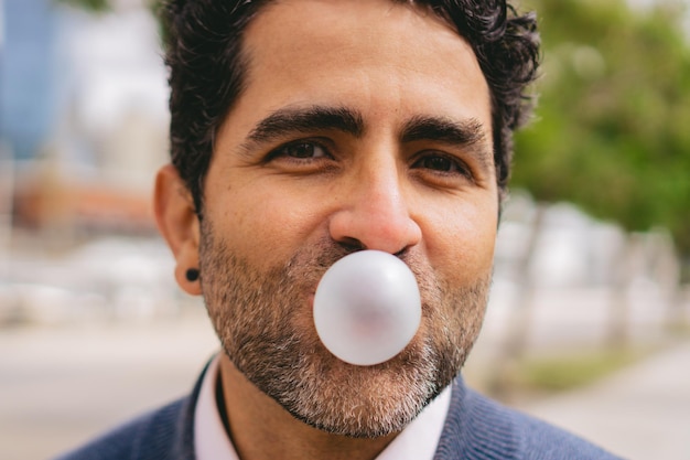 Close-up detail van een man van middelbare leeftijd die een bel blaast met kauwgom terwijl hij naar de camera kijkt