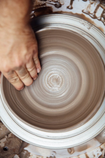 Foto chiuda sulla vista del dettaglio ad un artista rende le terraglie dell'argilla su una ruota di rotazione