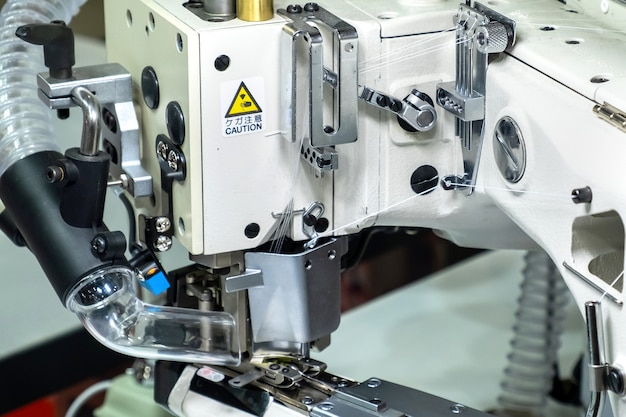 Close-up of details of modern white professional electric sewing machine on a table in factory. Work place of seamstress. No People.