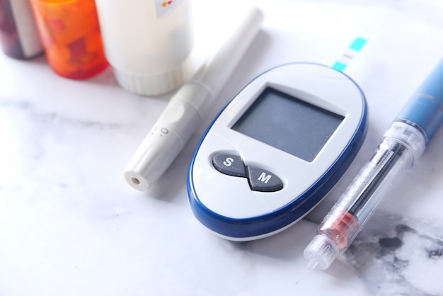 Закройте инструменты измерения диабета, инсулин и таблетки на белой поверхности