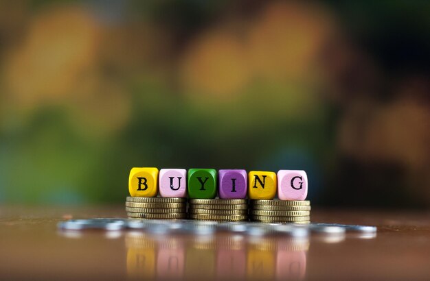 Photo close-up of dices with buying text over coins on table