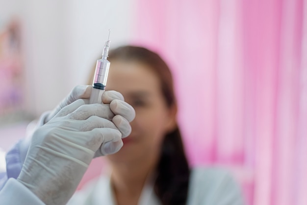 Close-up die van een vrouwelijke arts is ontsproten die een spuit houdt om voor te bereiden op de injectie van de geduldige zitting met een spannende blik