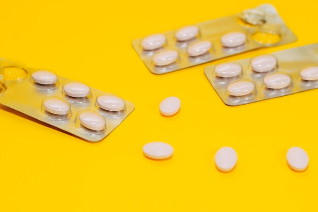 Close-up of different pills and vitamins are scattered on a yellow background, pills in a pack