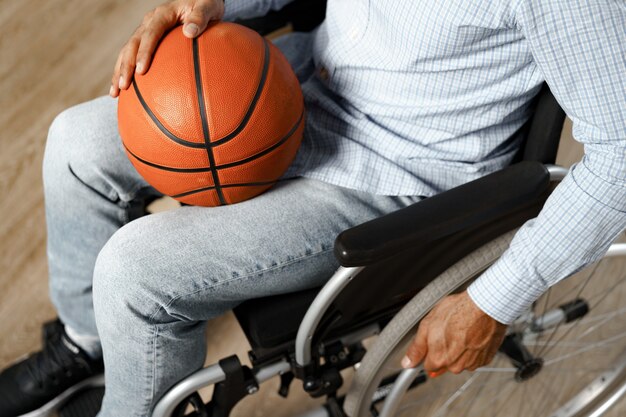 Primo piano di un uomo disabile seduto su una sedia a rotelle e che tiene in mano una palla da basket