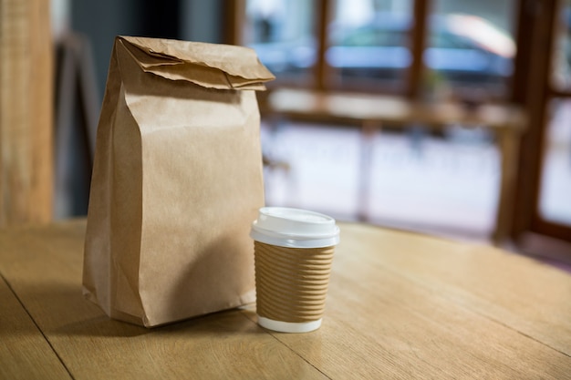 Close-up of disposable coffee cup and paper bag on table in cafe