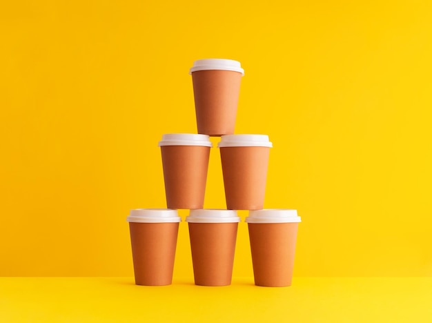 Close-up of disposable coffee cups arranged against yellow background