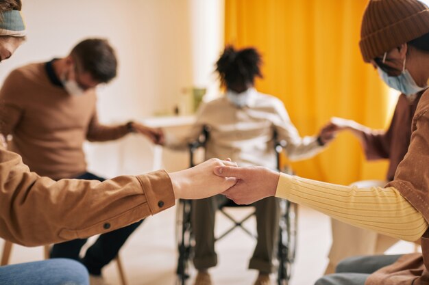 Foto primo piano di diversi gruppi di persone che si tengono per mano nel cerchio di supporto durante la sessione di terapia, tutti indossano maschere, copia spazio