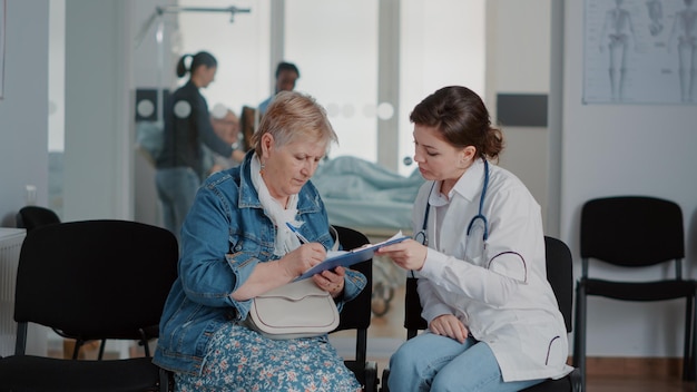 Close up of doctor giving medical advice to senior woman in\
waiting room lobby at clinic. general practitioner talking to\
pensioner about diagnosis and healthcare treatment at\
facility.