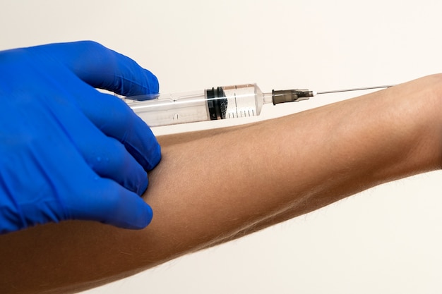 Close up of doctor hand in blue protective glove making injection with syringe to a patient.