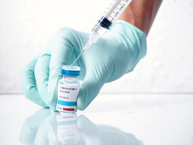 Photo close-up doctor hand extracting the covid-19 vaccine from a vial, white background.