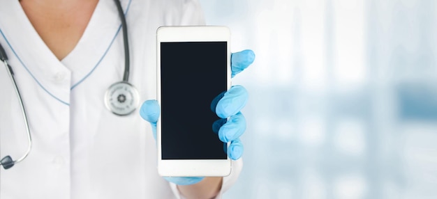 Закройте вверх руки доктора в медицинских перчатках, показывая приложение экрана пустого смартфона. Макет. Скопируйте место для вашего текста