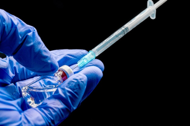 Close up of Doctor hands preparing the syringe and vial, for vaccination, on black isolated background.