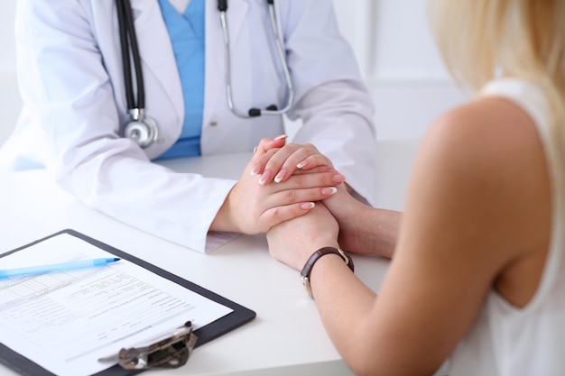 Close up of doctor hands reassuring her female patient. Medicine, help and health care concept