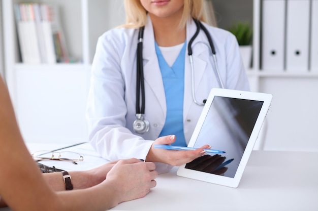 医師がタブレットコンピューターのモニターを指している間、医師と患者の手のクローズアップ。医学とヘルスケアの概念