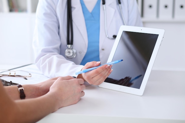 Close up of a doctor and  patient hands while phisician pointing into tablet computer monitor. Medicine and health care concept