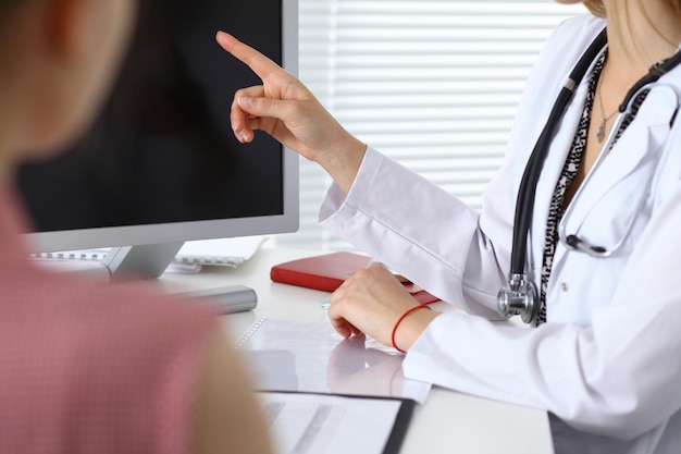 Close-up of a doctor and patient sitting at the desk while physician pointing into monitor computer. Medicine and health care concept.