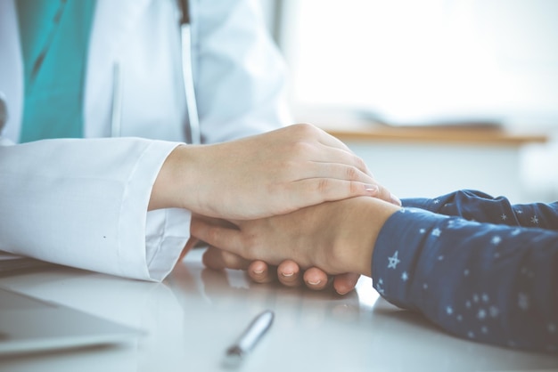 Close-up of doctor reassuring her female patient. Medical ethics and trust concept.