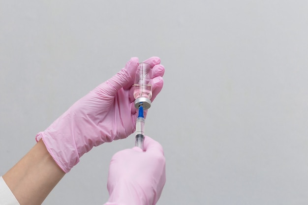 Крупным планом руки врача с бутылкой и вакциной, вакцина набирается в шприц. Медицинская концепция вакцинации лечение подкожной инъекцией, профилактика. На белом фоне.