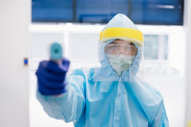 Foto primo piano di medico che indossa ppe tuta uniforme pronta per l'uso pistola termometro per controllare la temperatura corporea