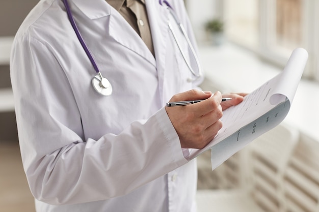 Close-up of doctor in white coat filling medical card with pen at the hospital