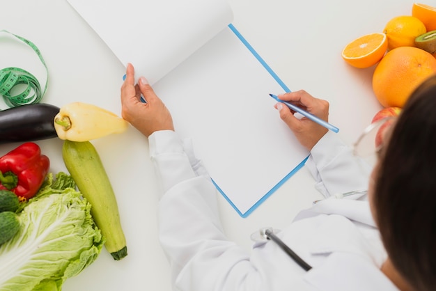 Close-up doctor with fruits and vegetables writing 