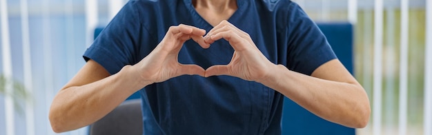 Close up of doctor working laptop and showing heart with hands in medical office