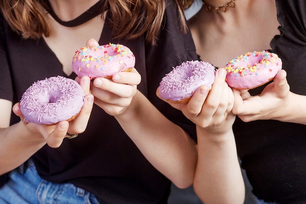 Закройте вверх пончики в руках девушки. Две девушки держат свежие красочные пончики