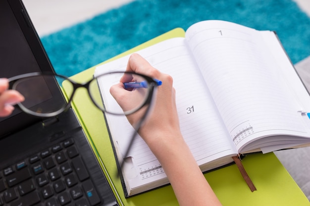 Close-up door een bril naar de open blanco pagina van een zakelijk dagboek of dagboek met een focus op de hand van de vrouw, die een pen vasthoudt voor het maken van afspraken, het organiseren van een schema of agenda