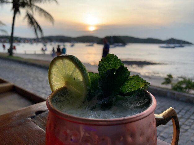 Photo close-up of drink against sea at sunset