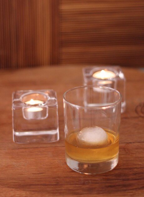 Photo close-up of drink in glass with lit tea light candles on table