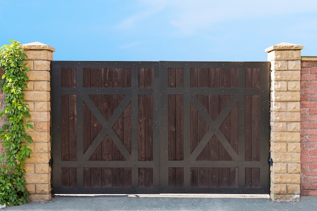 Photo a close up of a drive away dark wood closed gates at the clear blue sky background. entry gate of a country house. driveaway gates design idea. timber gates on the bricked fence. gates construction.