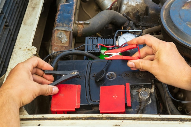 Primo piano delle mani del conducente che caricano la vecchia batteria dell'auto utilizzando l'elettricità attraverso i cavi jumper