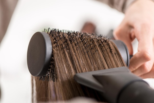 Foto primo piano di capelli castani che si asciugano con asciugacapelli e spazzola rotonda.
