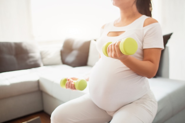 Close-up on a dumbbell. Pregnant woman with dumbbells. Active sporty life, wellness.