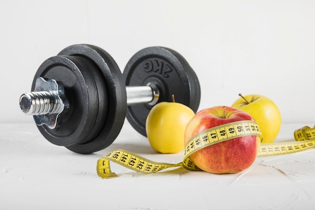 close-up of dumbbells and fruits with measuring tape on white background